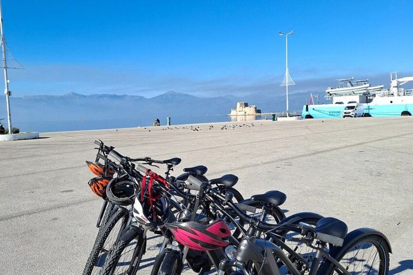 A concrete area with bicycles parked, a clear sky, and a distant view of mountains and a body of water. 2