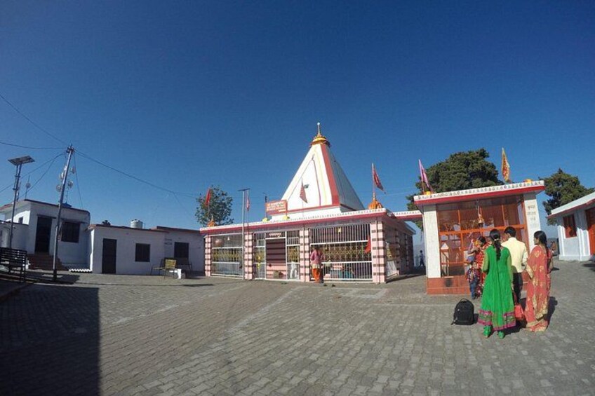Un templo con techo rojo y paredes blancas, rodeado de una zona pavimentada con gente. 5