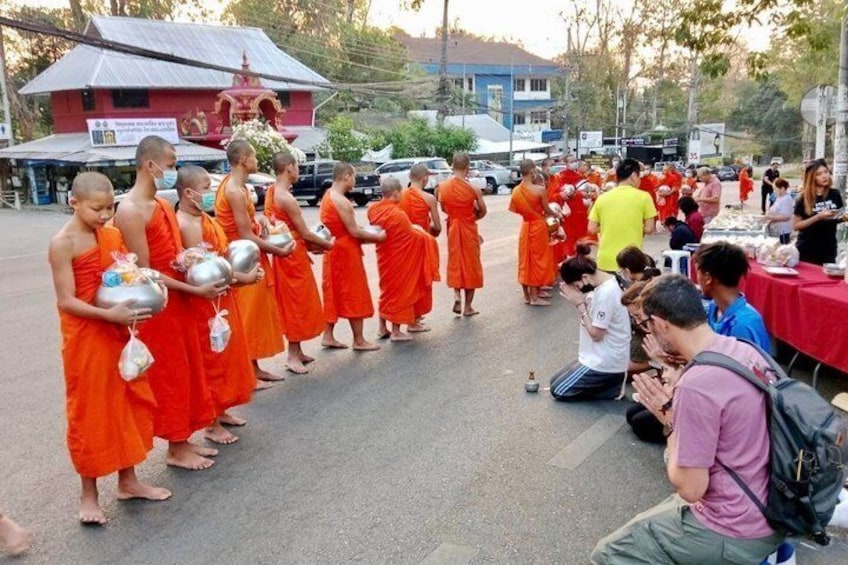 Monks in orange robes lined up on a street, some holding bowls. 1
