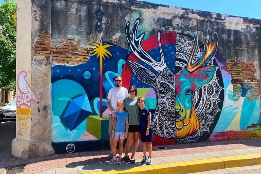 A mural with a deer and abstract patterns, a yellow curb, and a building with graffiti. 2