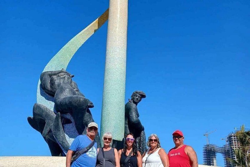 A group of people posing in front of a sculpture with a curved structure and two animal figures. 5