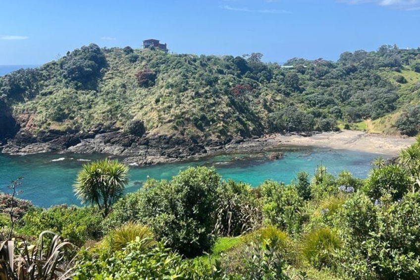 Paisaje costero con playa, vegetación exuberante y una colina con una edificación en la cima. 5
