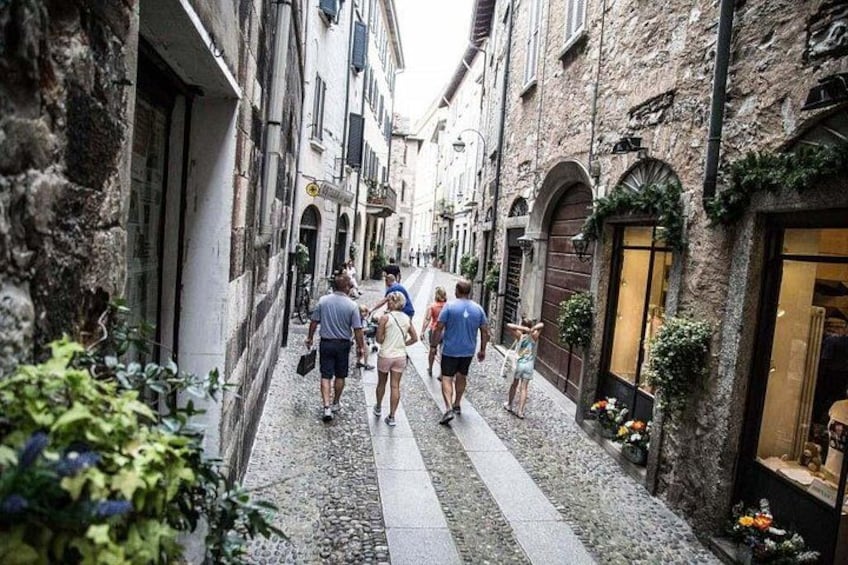 Una calle estrecha con peatones, edificios de piedra y una tienda con un escaparate grande. 2