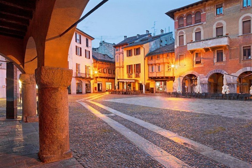 Una plaza adoquinada con edificios históricos, una columna de piedra y un ambiente cálido en la noche. 3