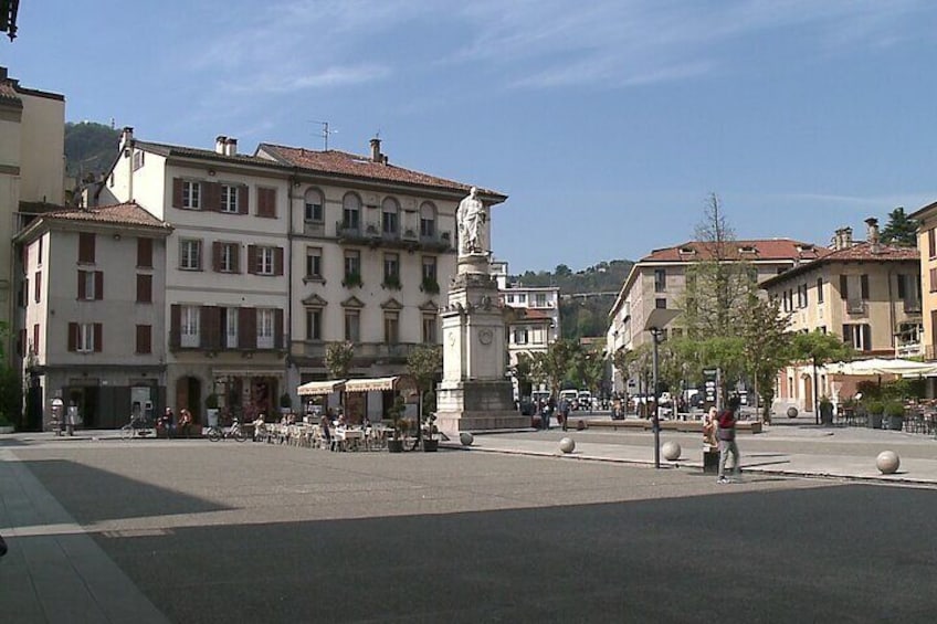Una plaza con un monumento central, edificios circundantes y zonas de estar al aire libre. 3