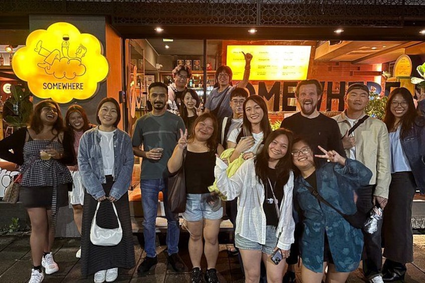 A group of people posing in front of a restaurant with a sign that reads 'SOMETHERE.' 5