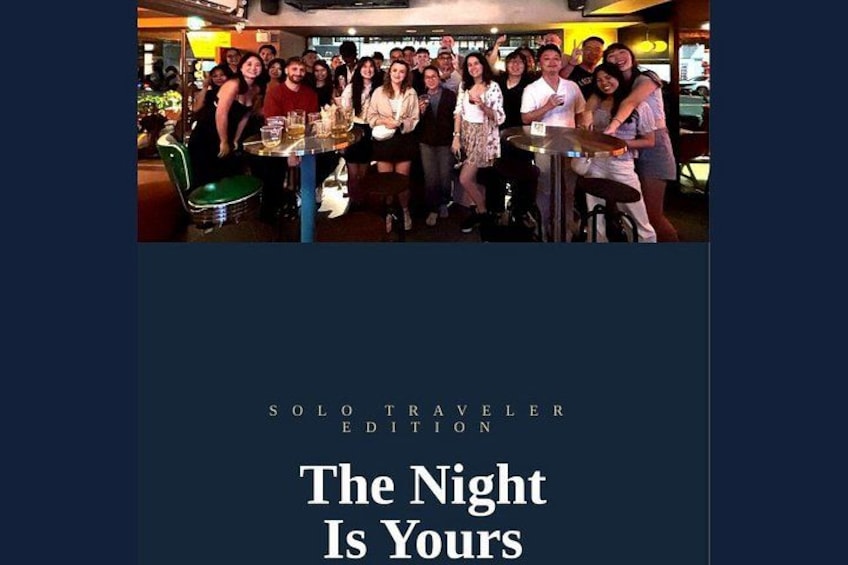A group of people at a bar with a sign that reads 'SOLO TRAVELER EDITION The Night Is Yours'. 2