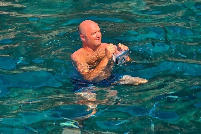 A person swimming in clear water, holding a snorkel and mask. 3