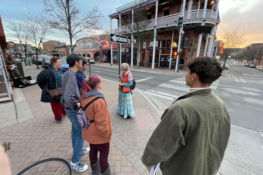 A group of people standing on a sidewalk near a street intersection with a building in the background. 3