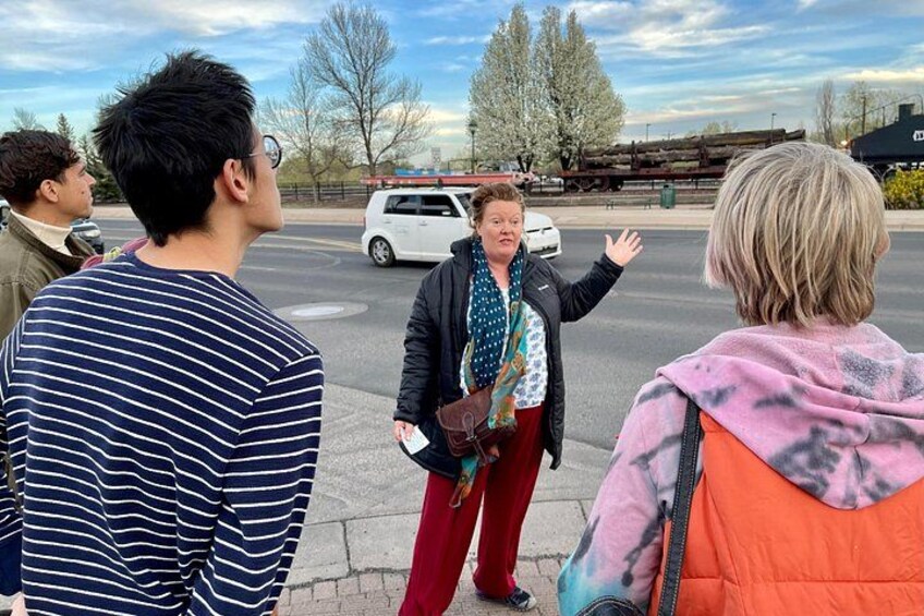 A group of people standing on a sidewalk, a white van in the background, and a building with a red roof. 4