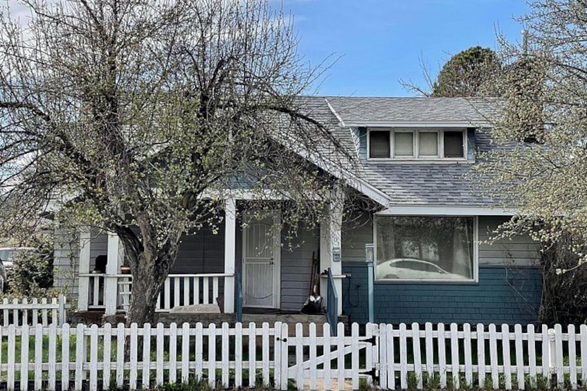 A single-story house with a porch, a white picket fence, and a tree in front. 5