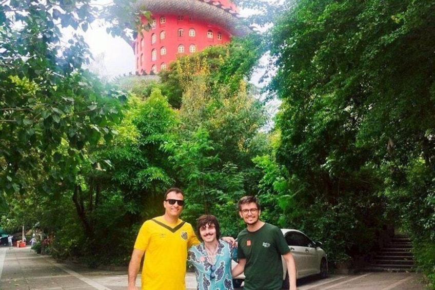 Three people standing in a lush green area with a red building in the background. 2