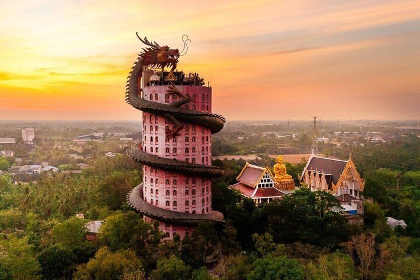 Ein mehrstöckiger Turm mit einem Drachen auf der Spitze, umgeben von traditioneller Bebauung und üppigem Grün. 1