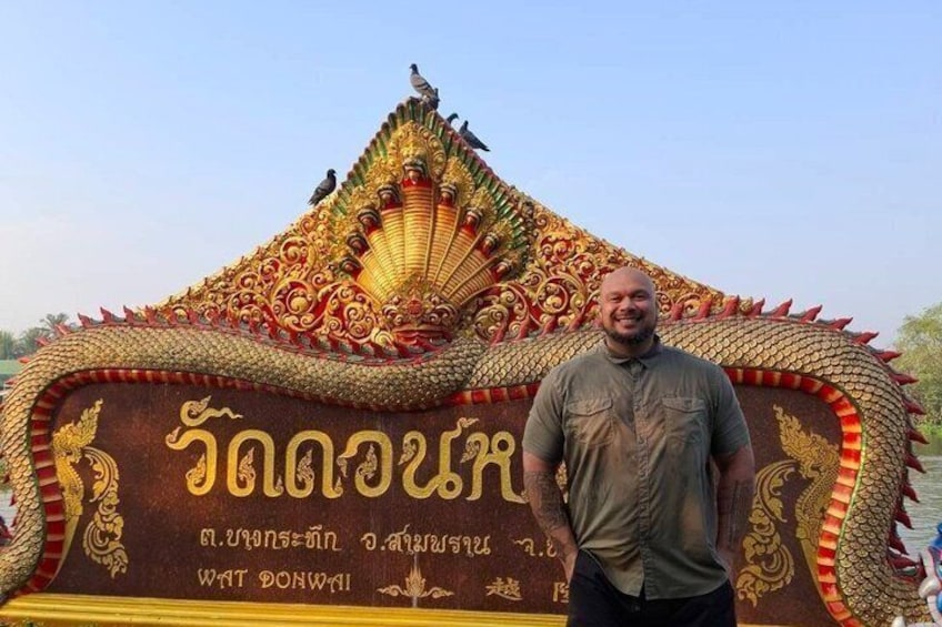 A man standing in front of a decorated structure with Thai script and a dragon motif. 4