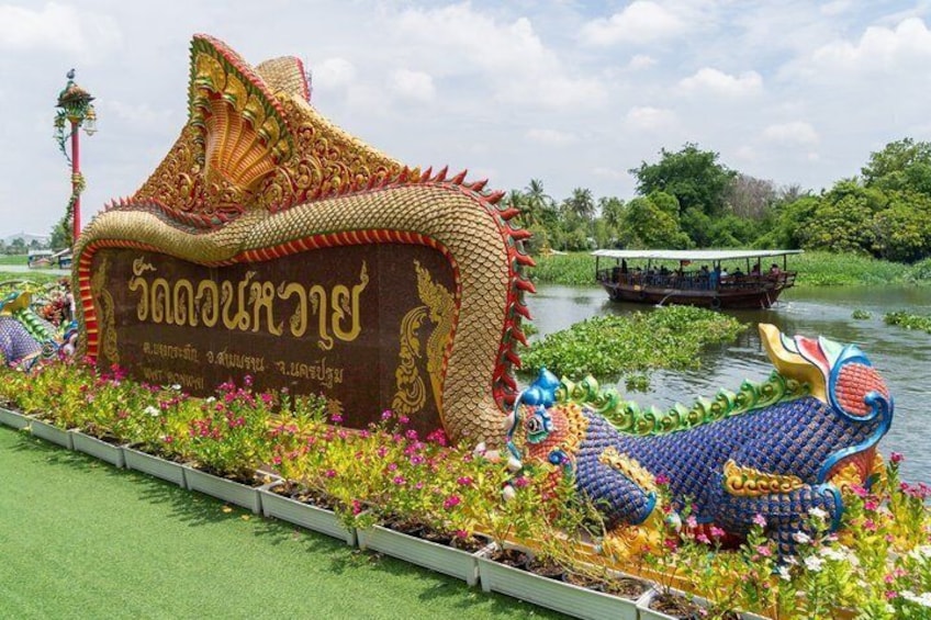 A dragon-shaped float on a river, surrounded by lush greenery and a boat in the background. 1
