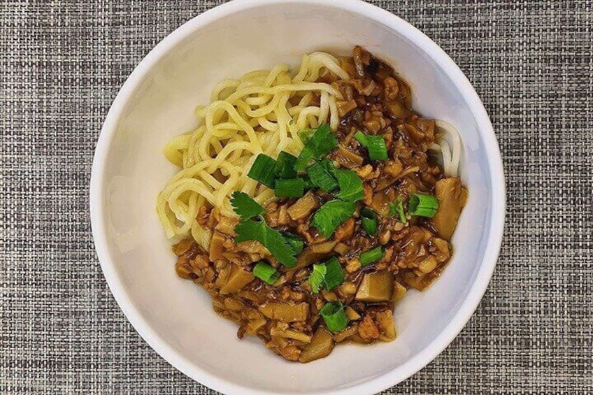 A bowl of noodles with a meat-based topping and garnished with green herbs. 3