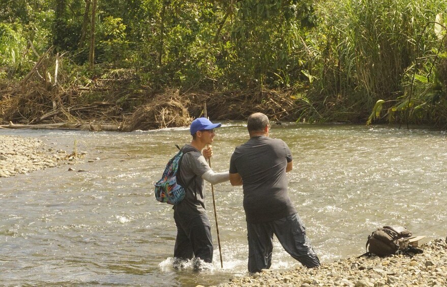 Two people wading in a river with a backpack and a walking stick. 5