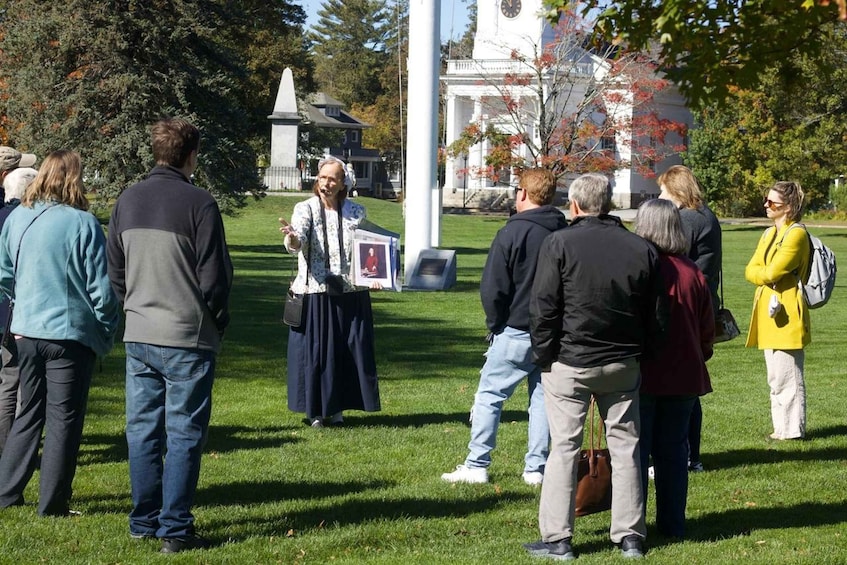 A group of people standing in a grassy area with a white building and a clock tower in the background. 1