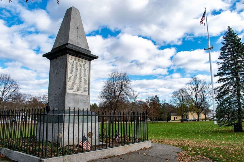 A monument with an inscription, surrounded by a black metal fence, American flags, and a flagpole with an American flag. 2