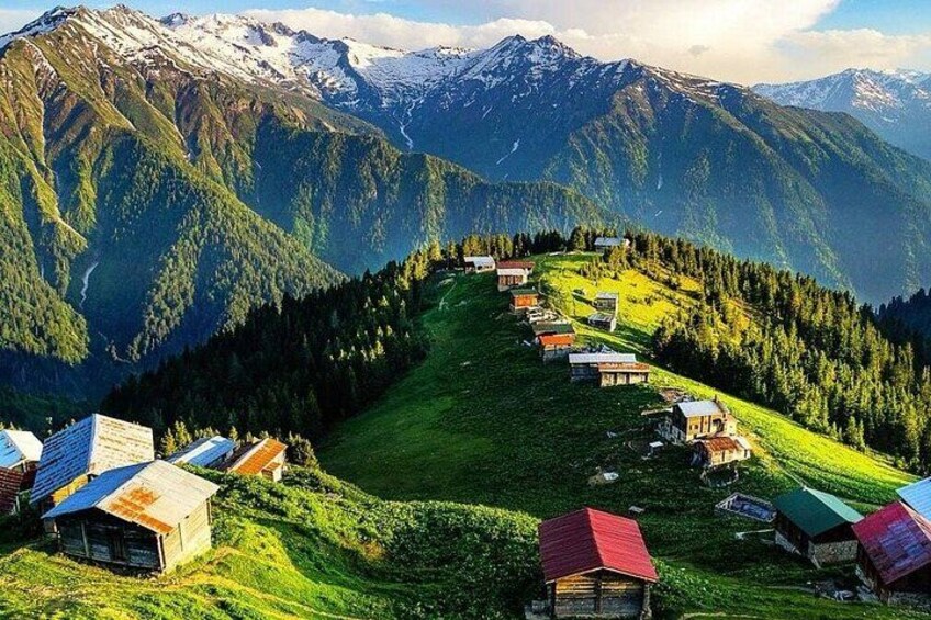 A mountain village with houses on a hillside, surrounded by snow-capped mountains. 1