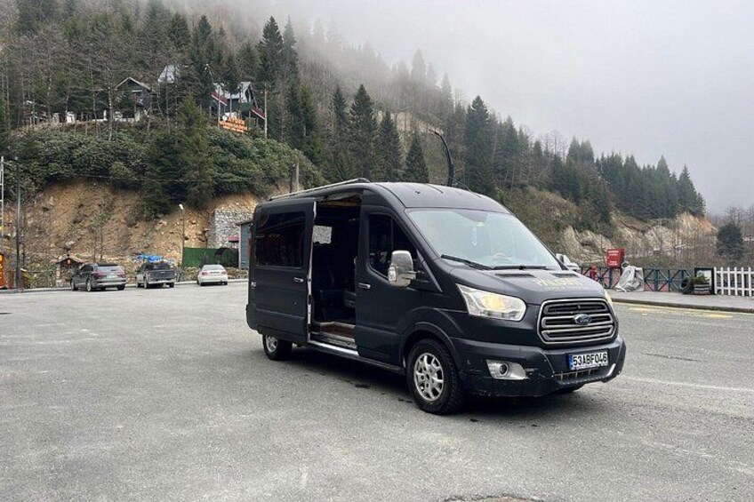 A black van parked on a road with a mountainous backdrop. 3