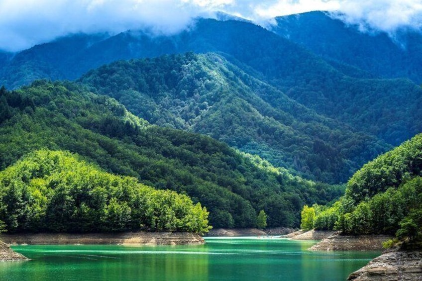A mountainous landscape with a clear lake surrounded by dense forest. 1