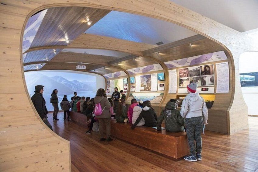 An indoor exhibit with wooden walls and a curved ceiling, displaying various informational panels and artifacts. 3