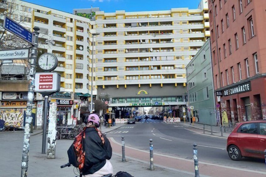 Eine Straße mit einem großen, gelben Gebäude, einer Uhr und einem roten Auto. 4
