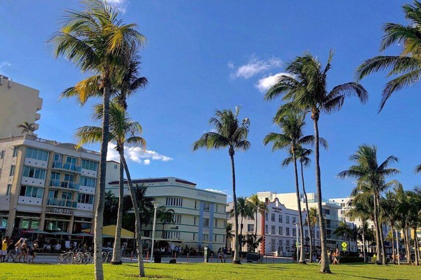 Una zona urbana assolata con palme, un hotel e persone che passeggiano. 2