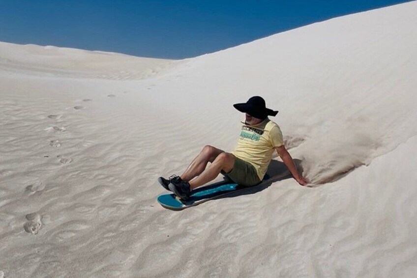 A person sitting on a blue sled in a sandy area with footprints. 2