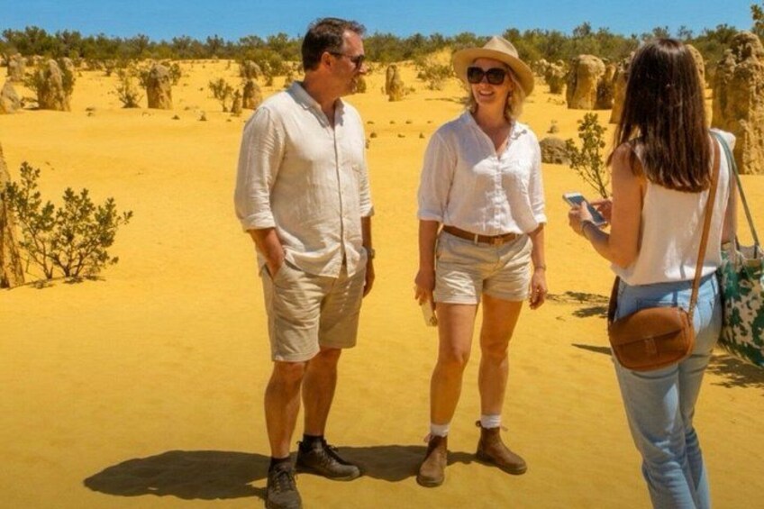 Three people standing in a desert with sand dunes and sparse vegetation in the background. 1