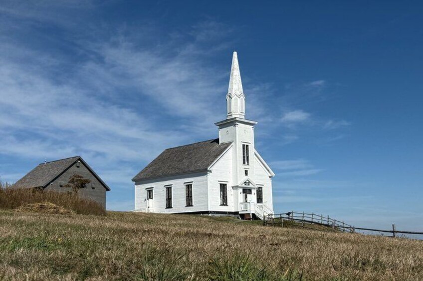 A white church with a steeple, a wooden fence, and a grassy field. 1