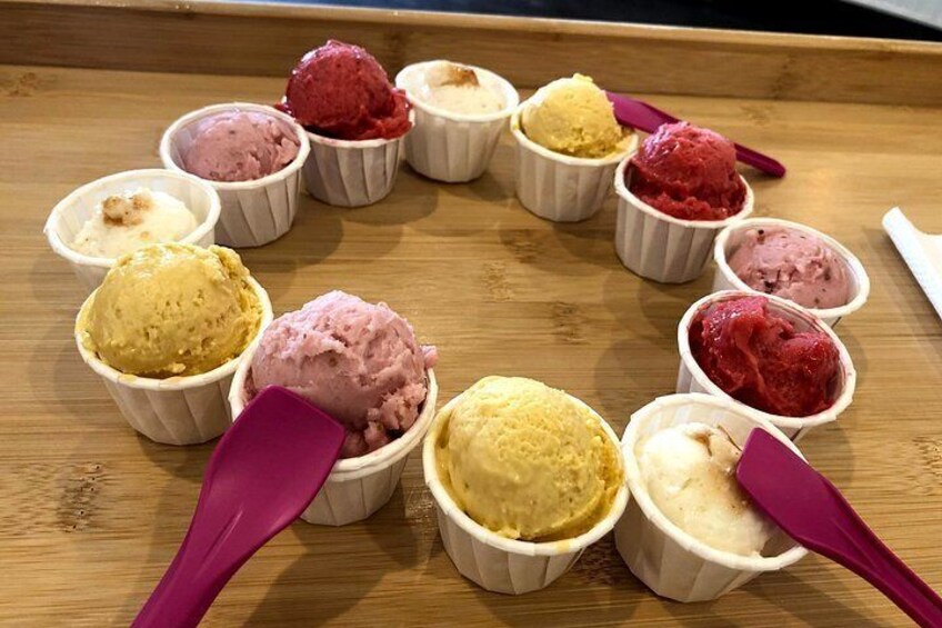 A wooden tray with multiple small cups of ice cream in various colors. 1