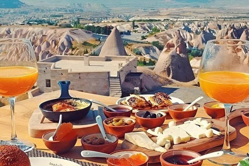 A table with food and drinks, set against a backdrop of a mountainous landscape. 1