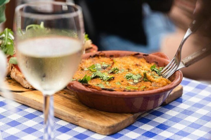 A dish in a terracotta bowl on a checkered tablecloth, accompanied by a glass of white wine. 3