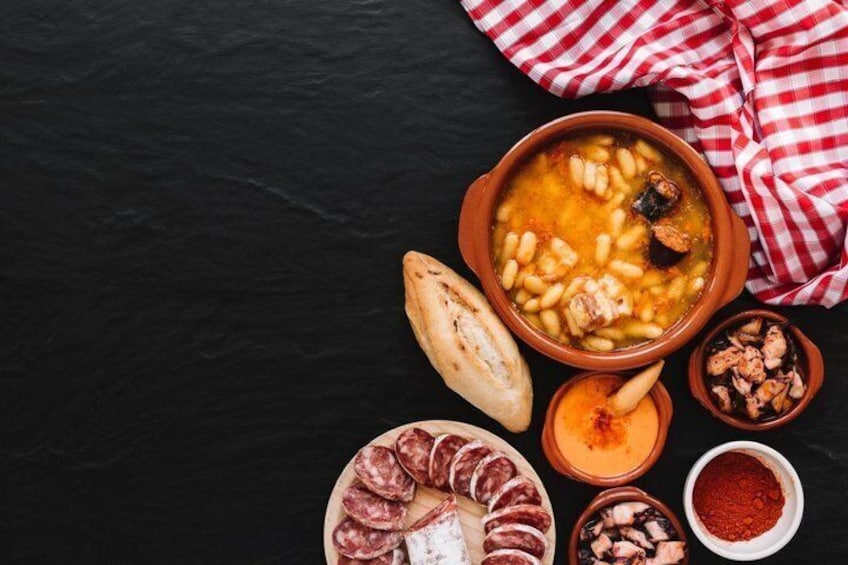 A bowl of bean soup with a piece of bread and a plate of cured meats. 2