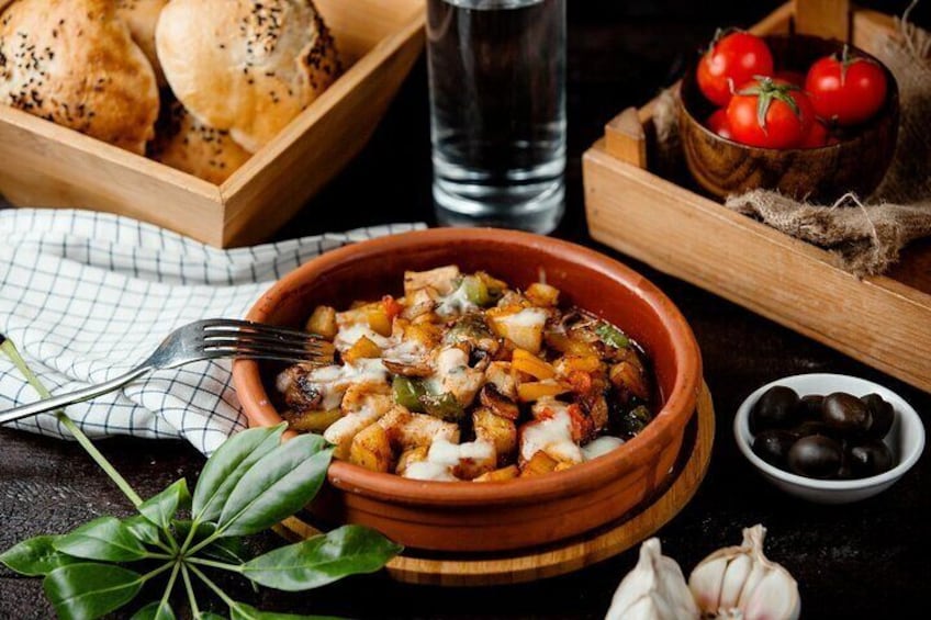A bowl of food with vegetables and cheese, a glass of water, and a basket of bread. 1