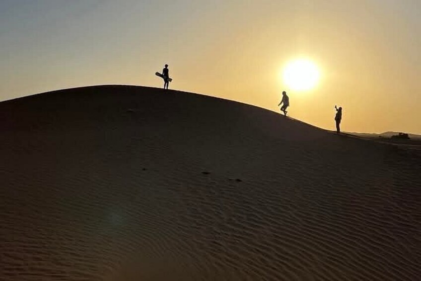 A desert landscape with two people standing on a sand dune, silhouetted against a sunset. 3