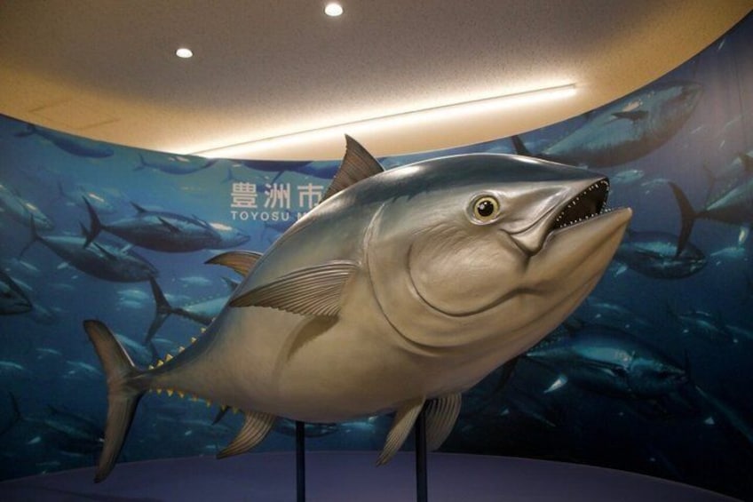 Una gran escultura de pez en una exhibición interior, con un fondo de escenas submarinas y texto. 3