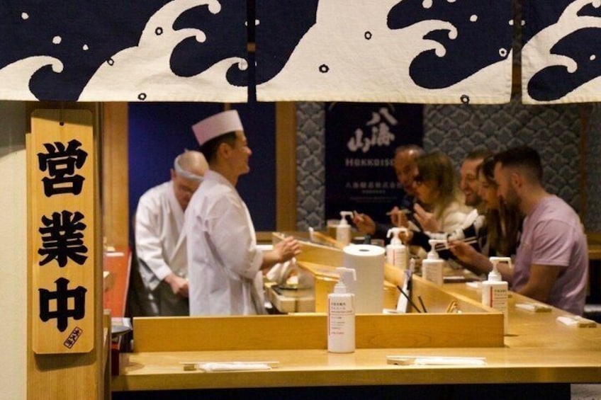 Interior de un restaurante de sushi con barra, paneles de madera y un letrero con caracteres japoneses. 1