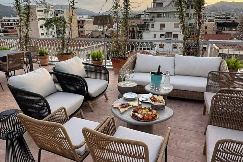 Een terras op het dak met rieten meubels, een ronde tafel met eten en plantenbakken. 1