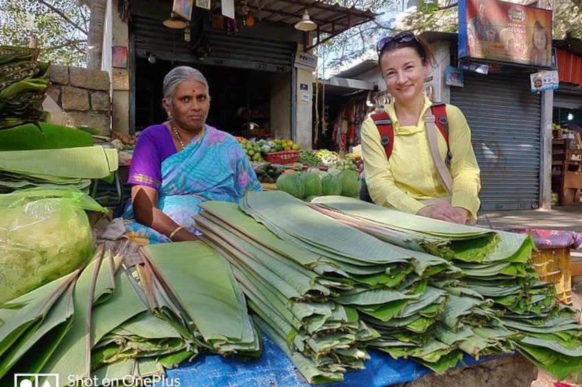 Dos personas sentadas a una mesa con hojas verdes grandes, posiblemente de plátano, en un mercado. 2