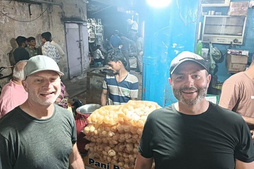 Dos hombres de pie en un mercado cubierto concurrido, con una gran pila de papas al fondo. 5