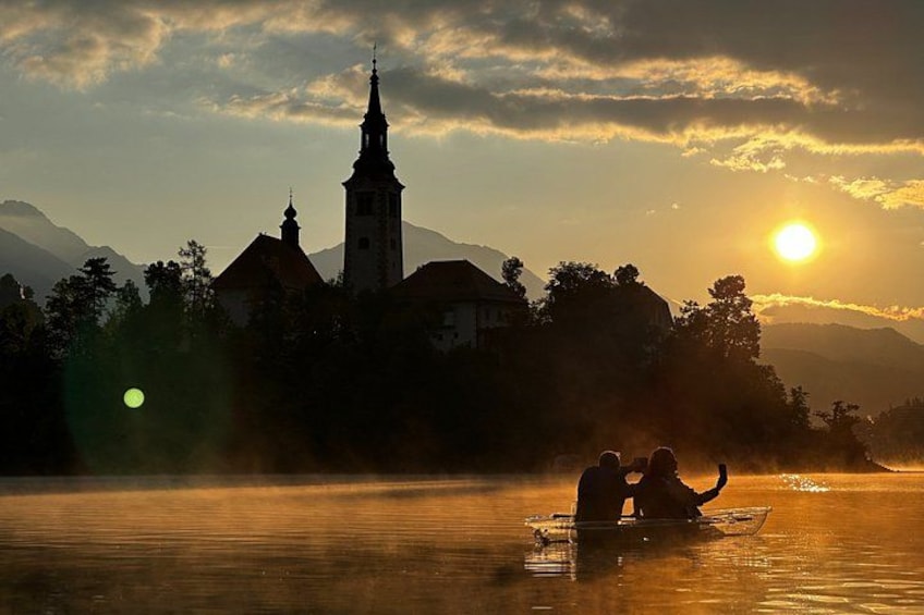 A sunset over a body of water with a church and mountains in the background. 2