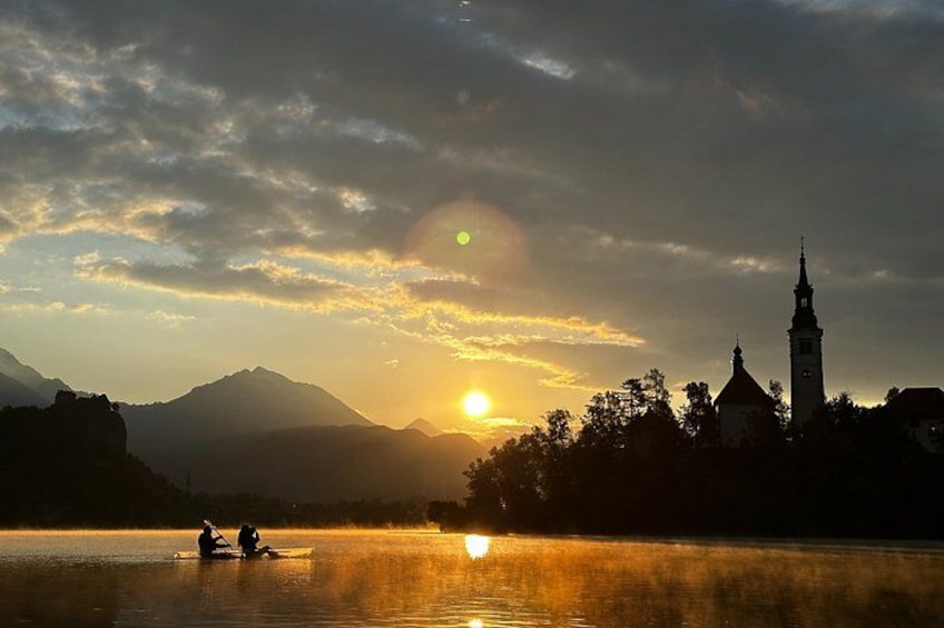 Un atardecer sobre un lago con una iglesia y montañas al fondo. 2
