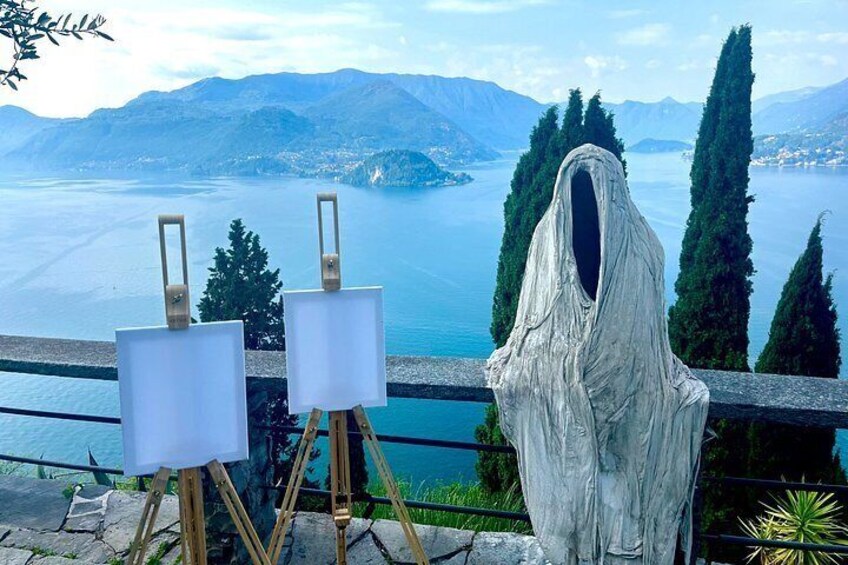 Eine Küstenlandschaft mit einer Statue einer geisterhaften Gestalt, zwei Staffeleien mit leeren Leinwänden und Blick auf das Meer und die Berge. 4
