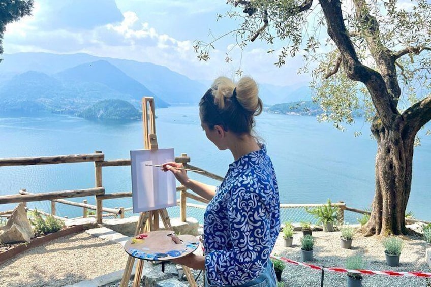 Eine Person malt an einem Staffelei am See, im Hintergrund sind Berge zu sehen. 5