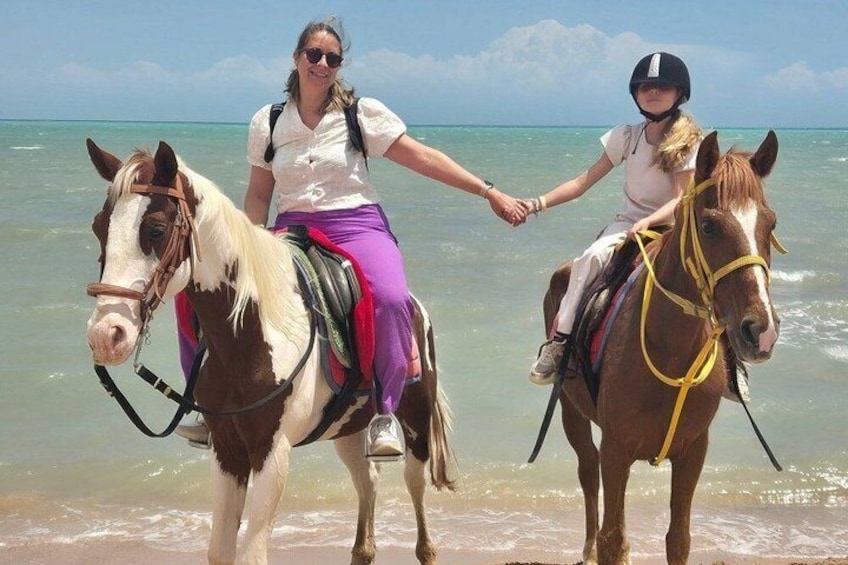 Dos personas cabalgando en una playa, con el océano al fondo. 1