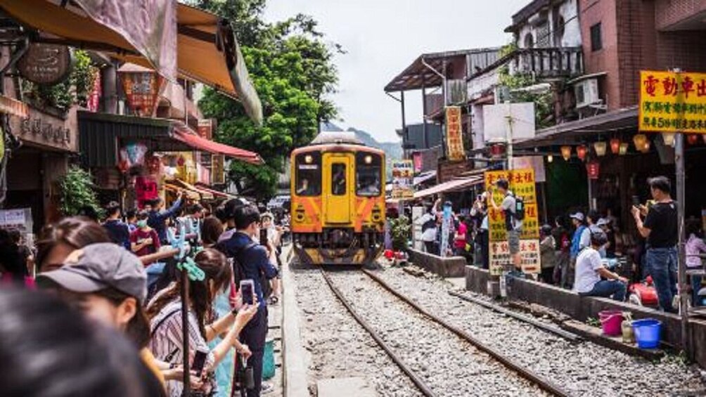 A train passing through a crowded street with shops and people on the sides. 3