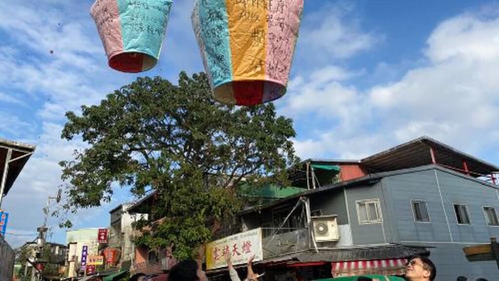 Colorful paper lanterns, a tree, and buildings in a street scene. 2